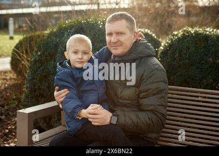Herbstliche Familienzusammenhänge: Vater, 40 Jahre alt, und Sohn - wunderschöner 8-jähriger Junge, im Park sitzend. Stockfoto