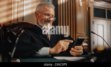 Gerichtshof und Gerichtshof zu einer Kaffeepause: Lächelnder männlicher Richter mit Smartphone, Surfen in Online-Inhalten, Nutzung der Social Media App, Investitionen, Internet-E-Commerce-Käufe. Stockfoto