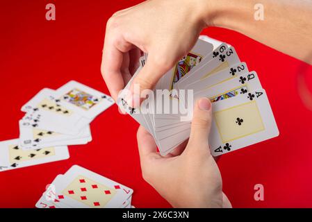 Brettspiel. Karten spielen. Pokerkarten in einer Hand eines jungen Mannes. Isoliert auf rotem Hintergrund. Stockfoto