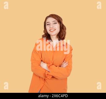 Junge kaukasische rote bob-Haare lächelnde selbstbewusste Frau. Er posiert Arme, steht über einem pastellorangen Atelierhintergrund. Glücklich, positiv, stolz. Stockfoto