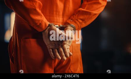 Filmische Nahaufnahmen eines mit Handschellen gefesselten Sträflings bei einem Prozess vor Gericht. Handschellen an den Angeklagten im Jumpsuit in Orange. Strafandrohter verurteilt, Gefängnisstrafe zu verbüßen. Stockfoto