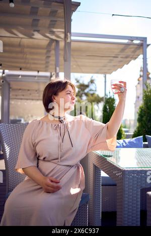 Eine mittelgroße Frau in pfirsichfarbenem Kleid mit einem Glas Wasser im Restaurant Stockfoto