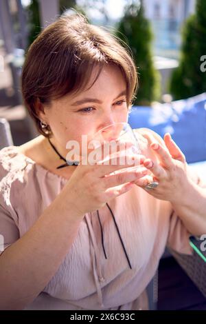 Eine mittelgroße Frau in pfirsichfarbenem Kleid mit einem Glas Wasser im Restaurant Stockfoto