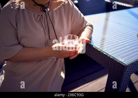 Eine mittelgroße Frau in pfirsichfarbenem Kleid mit einem Glas Wasser im Restaurant Stockfoto