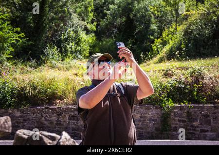 Ein einsamer männlicher Wanderer, der auf der Straße spaziert und die Gelegenheit nutzt, Sehenswürdigkeiten zu besichtigen, indem er unterwegs Fotos mit seinem Handy macht Stockfoto