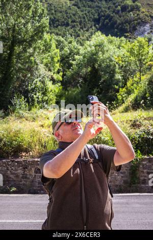 Ein einsamer männlicher Wanderer, der auf der Straße spaziert und die Gelegenheit nutzt, Sehenswürdigkeiten zu besichtigen, indem er unterwegs Fotos mit seinem Handy macht Stockfoto