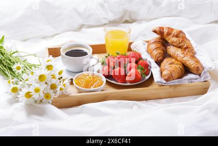 Frühstück im Bett. Tablett mit einer Tasse Kaffee, Croissants, Marmelade, Orangensaft, frischem Obst und Gänseblümchen Stockfoto