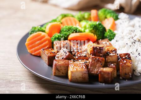 Nahaufnahme eines Tellers mit gebratenem Tofu, Reis und Gemüse mit Sesamsamen auf Holztisch Stockfoto