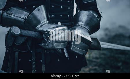 Mittelalterlicher Ritter trägt Rüstung und Helm, zieht Schwert aus Shearh, bereit zum Kampf, tötet seinen Feind in der Schlacht. Krieger Soldat auf dem Schlachtfeld. Krieg, Invasion, Kreuzzug. Filmische Historische Reenactment Stockfoto