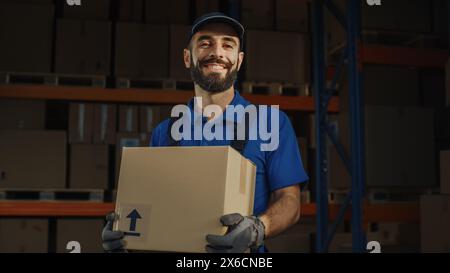 Porträt eines gutaussehenden männlichen lateinischen Arbeiters, der Pappkarton hält, der im Lager mit vollen Waren steht. Happy Professional arbeitet im Logistics Distribution Center und liefert E-Commerce Online-Bestellungen. Stockfoto