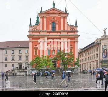 Touristen mit Sonnenschirmen auf dem Preseren-Platz, vor der Franziskanerkirche der Verkündigung, Ljubljana, Slowenien, an einem regnerischen Tag. Stockfoto