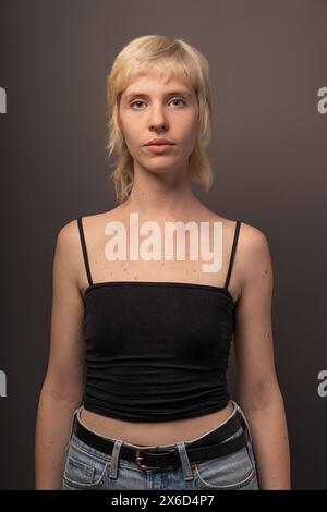Porträt einer blonden Frau in schwarzem Oberteil und Jeans, Studiofotografie mit Hervorhebung von Mode und persönlichem Stil, neutraler Hintergrund. Stockfoto