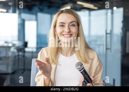 Lächelnde Geschäftsfrau mit Mikrofon während einer Präsentation in einem modernen Büro. Eine professionelle Frau hält eine Rede oder einen Vortrag. Stockfoto