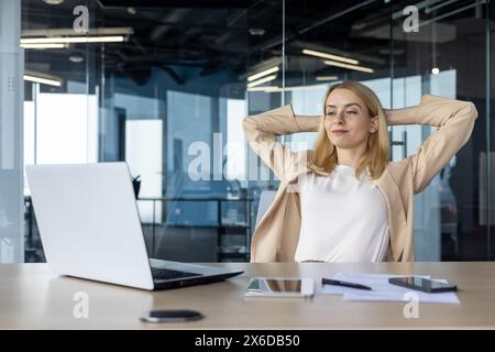 Eine professionelle Frau macht eine Pause an ihrem Arbeitsplatz und dehnt sich mit Zufriedenheit. Ein moderner Bürobereich ist die perfekte Kulisse für Produktivität und Entspannung. Stockfoto