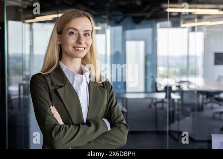 Eine junge, professionelle Frau mit einem angenehmen Lächeln steht selbstbewusst in einem modernen Bürostil, gekleidet in einem stilvollen grünen Blazer. Stockfoto