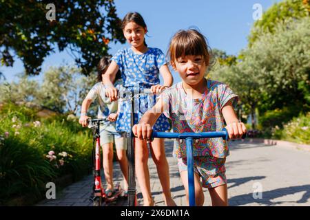 Aus nächster Nähe sehen Sie drei Kinder, die an einem sonnigen Tag mit Motorrollern fahren Stockfoto