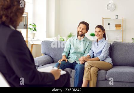 Glückliches, lächelndes junges Paar, das auf der Couch im Büro des Ratgebers sitzt, Ratschläge hört und lächelt. Stockfoto