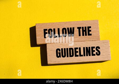Folgen Sie den Hinweisen auf Holzblöcken mit gelbem Hintergrund. Konzeptionell Befolgen Sie das Richtliniensymbol. Kopierbereich. Stockfoto