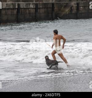 Ein Mann mit seinem Hund läuft im Meer entlang der Küste, Seixal, Madeira, Portugal Stockfoto