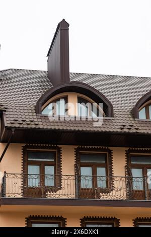 Das Dach des Hauses besteht aus roten Metallfliesen, einem wunderschönen großen Kamin. Stockfoto