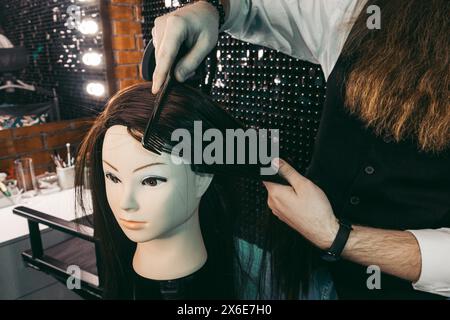 Friseurkämmpraxis am Schaufensterpuppen. Mann junger Friseur fleißig enthusiastisch mit langem Bart und Haaren in der Weste, kämmen Haarfrisuren Stockfoto