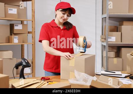 Paketverpackung. Postbeamte kleben Box an Holztisch drinnen Stockfoto