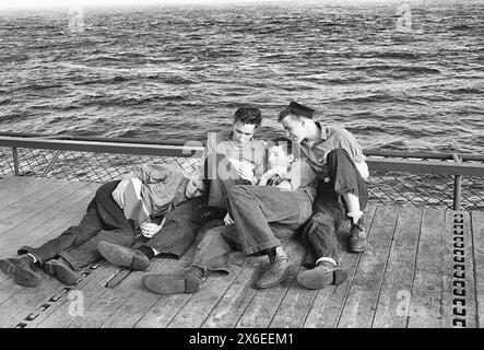 Eingesessene Männer, die am Rande des Fahrstuhls an Bord der USS Lexington (CV-16) lesen, November 1943 Stockfoto