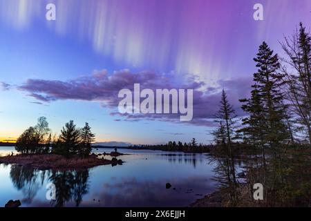 Nordlichter erstrahlen über einem See in Minnesota in einem dunklen Himmel über dem Himmel, während die Sonne am Horizont untergeht Stockfoto