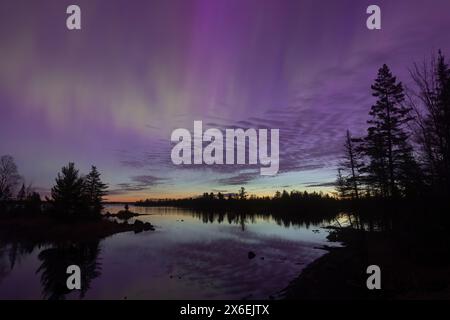 Nordlichter leuchten über einem See in Minnesota, während die Dämmerung am Horizont den leuchtenden Regenbogen des Aurora-Lichts ergänzt Stockfoto