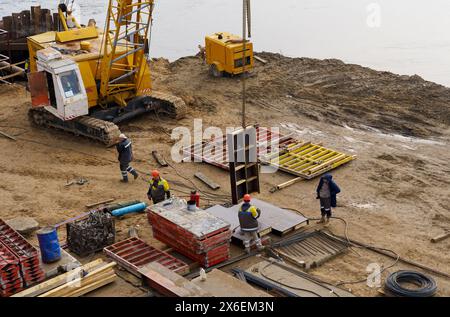 Bobruisk, Weißrussland - 29. Oktober 2022: Eine Gruppe von Männern beschäftigt sich mit dem Brückenbau und führt Aufgaben wie Aushubarbeiten mit einem Bagger aus. Stockfoto