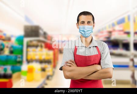 Geschäftseigentümer, der mit einer roten Schürze in einem Supermarkt arbeitet und eine Gesichtsmaske trägt, um das Coronavirus zu vermeiden - Pandemie-Lifestyle-Konzepte und Kopierraum. Stockfoto