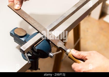 Man arbeitet mit einer Metallfeilschere aus Eisen oder Aluminium, die in einem Schraubstock auf dem Werkbanktisch in der Garagenwerkstatt gegriffen wird. Das Konzept „To it yourself“, Hände nah beieinander Stockfoto