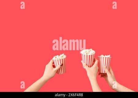 Hände halten Eimer mit Popcorn und auf rotem Hintergrund Stockfoto