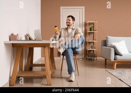 Junger Mann mit einer Flasche Zitronenwasser, der am Tisch im Büro sitzt Stockfoto
