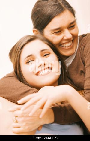 Eine Frau mittleren Alters mit einem Lächeln umarmt junge Erwachsene Tochter, die auf ihrem Schoß auf einer Couch liegt und Zuneigung zeigt Stockfoto