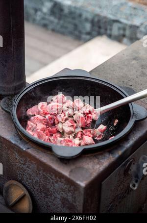 Mann, der Schweinefleisch und Rindfleisch in einem Kessel im Garten frittiert Stockfoto