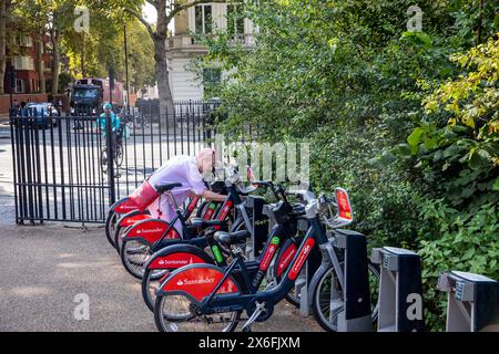 Hyde Park London Elektro-E-Bike-Verleih, Model freigelassen Frau Mitte 50 gibt den Zugangscode ein, um E-Bike aus dem Bike-Hub-Schloss im Zentrum von London zu entfernen Stockfoto