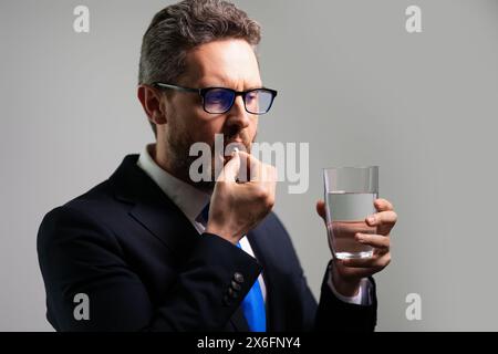 Arzneimittelpille bei Kopfschmerzmigräneerkrankungen. Mann mit Kopfschmerzen auf isoliertem grauem Atelierhintergrund. Der Mann fühlt Schmerzen, die trockene Augen von der Arbeit müde reiben. Stockfoto