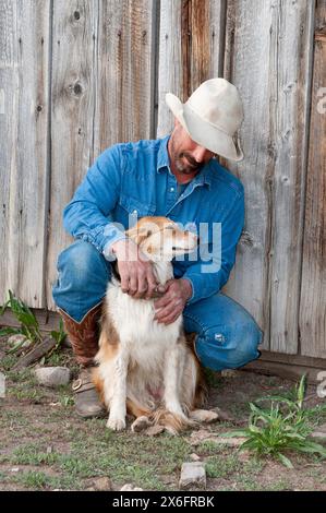 Cowboy mit australischem Hirten, der sich auf die Scheune lehnt (MR) Stockfoto