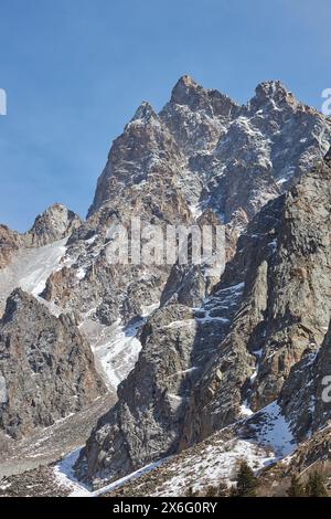 Raue, zerklüftete Berggipfel stehen unter klarem blauen Himmel. Der Gipfel ist teilweise mit Schnee bedeckt, was auf eine hohe Höhe und niedrige Temperaturen hinweist. Keine Vegetation, unzugänglicher Ort. Felsformationen Stockfoto