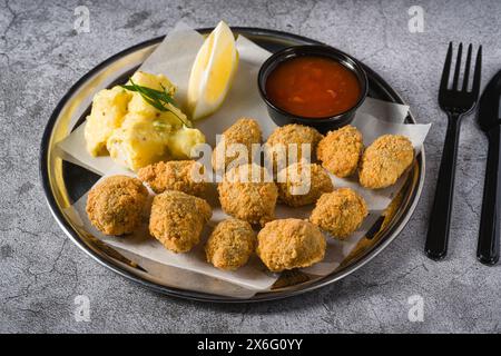 Gebratene Muscheln auf einem Metallteller mit Kartoffelsalat auf der Seite. Türkischer Name: Midye Tava Stockfoto