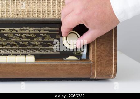 Echtes Radio aus den 50er - 60er Jahren Auf einem weißen Tisch. Zeitspuren. Die Hand eines Mannes auf dem Radiowell stellt die Welle ein. Nahaufnahme Stockfoto