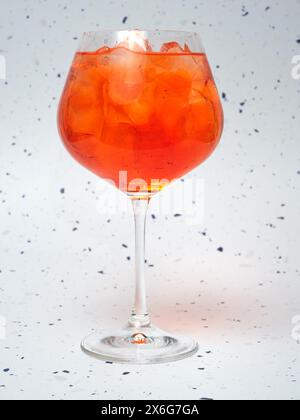 Eine Nahaufnahme eines gekühlten Aperol Spritz gefüllt mit Eiswürfeln. Das lebhafte Orangengetränk hebt sich vor einem gesprenkelten Hintergrund ab. Stockfoto