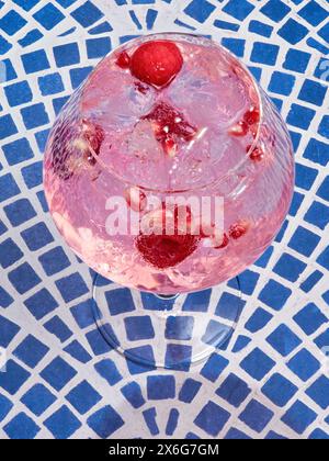 Eine Nahaufnahme eines erfrischenden rosafarbenen Gin Tonic gefüllt mit Eis und Beeren vor blauem Hintergrund. Stockfoto