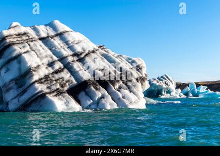 Ein großer Eisblock befindet sich im Ozean, umgeben von kleineren Eisblöcken. Eisberg zeigt Schichten unterschiedlicher Farben aufgrund jahrelanger Sedimentierung. Die sce Stockfoto