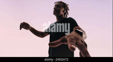 Ein junger Mann mit Dreadlocks tanzt energisch zum Rhythmus eines Liedes in einem Studio-Hintergrund. Seine geschlossenen Augen und seine anmutigen Hände zeigen seine Leidenschaft Stockfoto