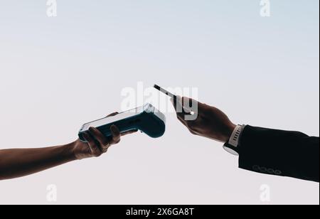 Der Kunde hält ein Smartphone in der Nähe eines Kassensystems und verwendet eine Bank-App, um zu tippen und zu bezahlen. Diese elektronische Zahlungstransaktion unterstreicht die Einfachheit und den Erfolg Stockfoto