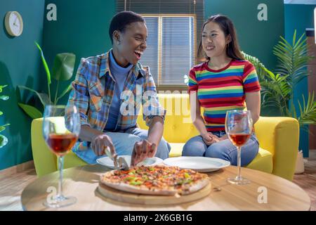 Zwei Freundinnen feiern mit Pizza und Wein und haben zu Hause Spaß Stockfoto