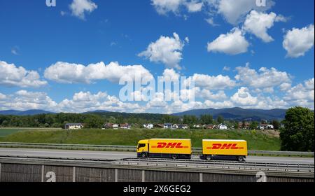 Ein gelber Lkw mit DHL-Logo fährt auf einer Autobahn bei Deggendorf mit Bayerischem Wald im Hintergrund, Niederbayern Stockfoto