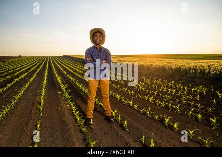 Ein afrikanischer Bauer steht auf seinem wachsenden Maisfeld. Er ist zufrieden mit dem Fortschritt der Pflanzen. Stockfoto